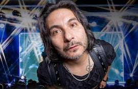 Felipe Avello con cabello largo y oscuro, en camiseta negra, mirando intensamente a la cámara con luces brillantes de fondo.