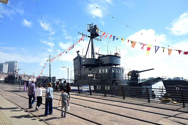Grupo de seis personas camina por el muelle, disfrutando del evento con barcos decorados de fondo.