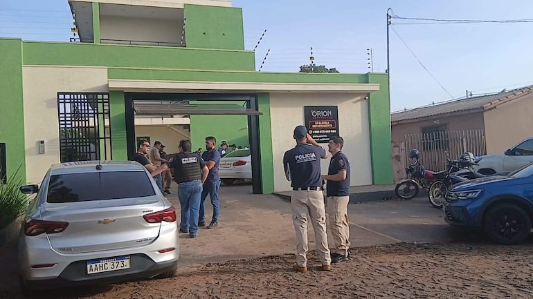Tres policías discuten en un edificio verde y blanco mientras conversan otros tres individuos en un entorno tranquilo.