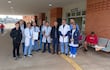 Grupo de médicos en batas blancas y uniformes azules se agrupan frente a un hospital durante una protesta, uno sostiene un papel.