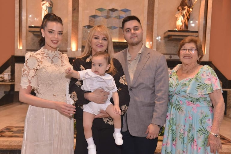 Grupo de cinco personas sonrientes: mujer joven con vestido claro, mujer con blusa negra, hombre en traje claro y mujer mayor con vestido floral.
