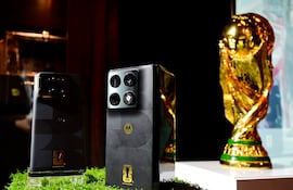 Dos teléfonos Motorola sobre mesa decorada con césped sintético, junto a la brillante Copa Mundial de la FIFA.