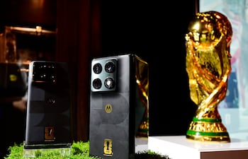 Dos teléfonos Motorola sobre mesa decorada con césped sintético, junto a la brillante Copa Mundial de la FIFA.
