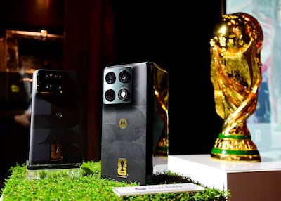 Dos teléfonos Motorola sobre mesa decorada con césped sintético, junto a la brillante Copa Mundial de la FIFA.
