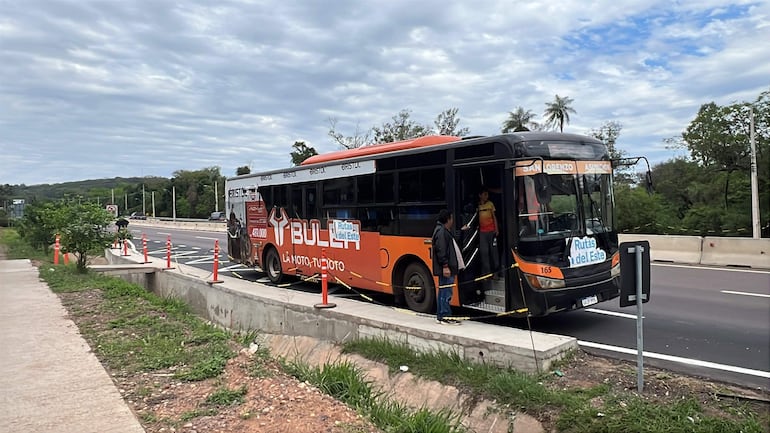 Autobús negro y naranja de BULI deteniéndose, con pasajeros cerca y un día nublado en la vía pública.