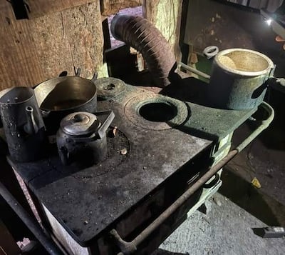Cocina rural con fogón de hierro desgastado, olla metálica y tetera sobre una superficie sucia.