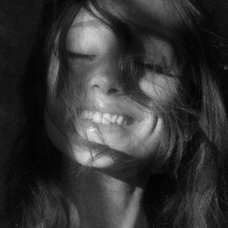 Ariana Grande muestra una gran sonrisa, luciendo un atuendo atractivo, con expresión de felicidad en un entorno vibrante.