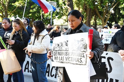 Mujer con cartel que dice 'QUE PAGUEN LOS RESPONSABLES, NO LAS VÍCTIMAS', rodeada de manifestantes y vegetación en un parque.