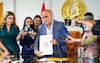 Basilio Núñez sostiene un documento, acompañado por mujeres reporteras en un entorno de prensa formal.