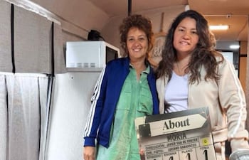 Shirley Giménez con chaqueta azul y camiseta verde, junto a Coral Gabaglio en chaqueta beige, sosteniendo cartel de producción.