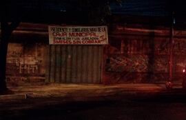 Cartel en pared denuncia que jubilados no cobran sus haberes, entorno urbano iluminado tenuemente.