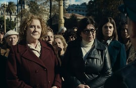 Seis mujeres de pie en un ambiente exterior, algunas con abrigos y chaquetas, escuchan atentamente a un hombre que les habla.
