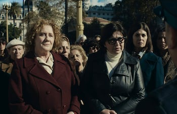 Seis mujeres de pie en un ambiente exterior, algunas con abrigos y chaquetas, escuchan atentamente a un hombre que les habla.