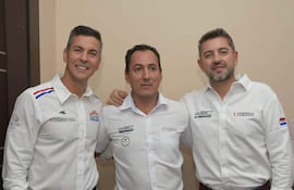 Óscar Martínez sonríe en camisa blanca, junto a Santiago Peña y Pedro Alliana, en un entorno institucional con fondo claro.