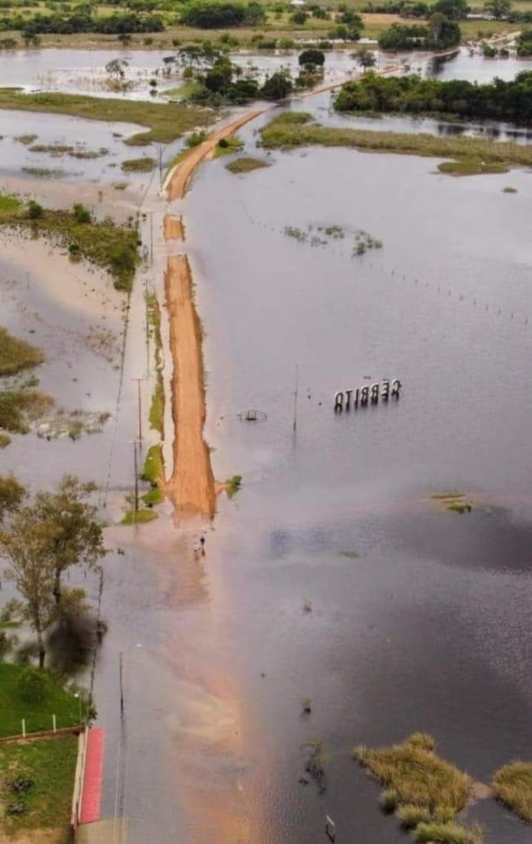 Cartel de 'CERRITO' sobresale del agua, rodeado de vegetación y un camino de tierra parcialmente inundado.