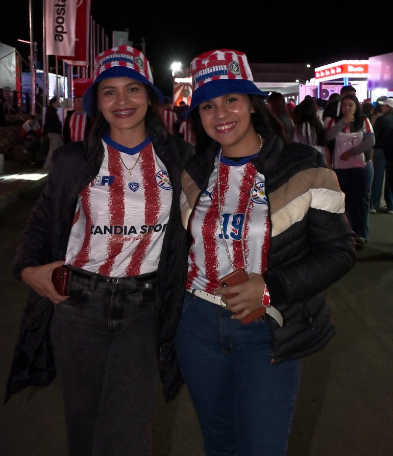 Dos mujeres con camisetas rojas y blancas, sonriendo. Fondo festivo con otras personas también vestidas del club.