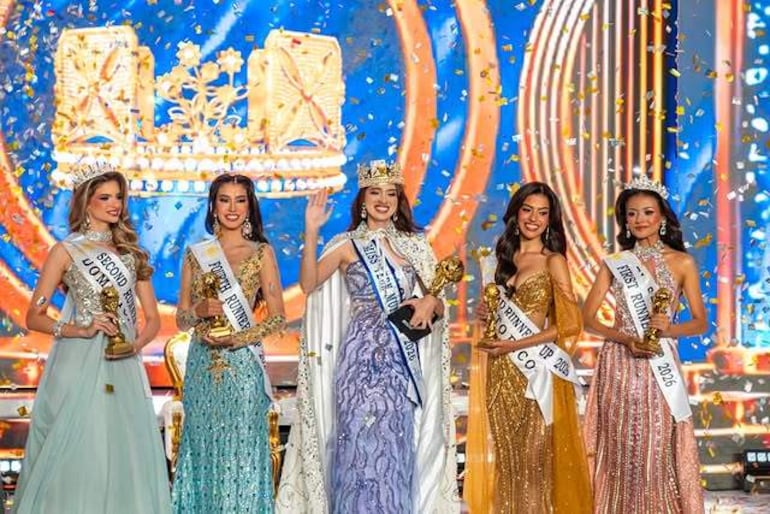 Cinco mujeres en trajes de gala, sonriendo y sosteniendo trofeos en un escenario decorado con confeti.
