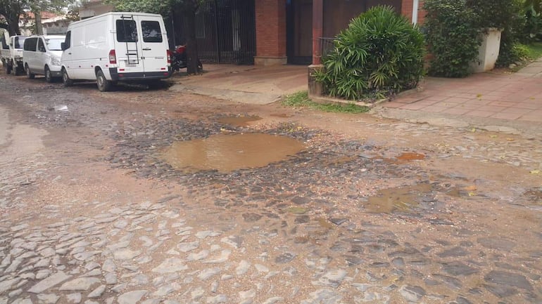 Calle adoquinada de Empedrado con charca de agua y furgonetas estacionadas en un entorno urbano.