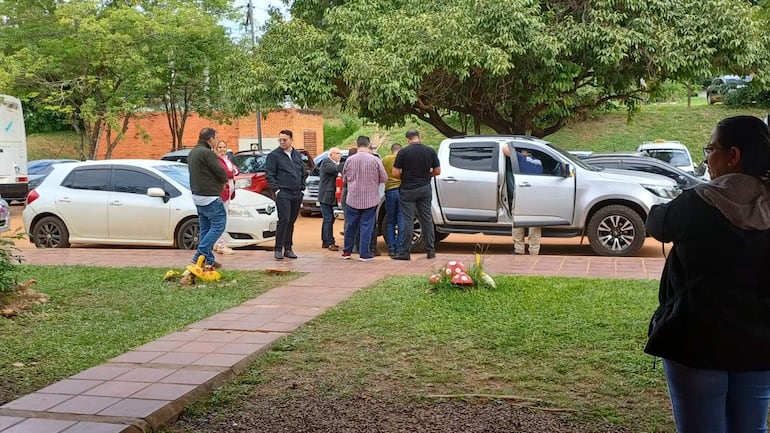 Siete personas conversan en un área verde, con un hombre hablando y un automóvil plateado al fondo.