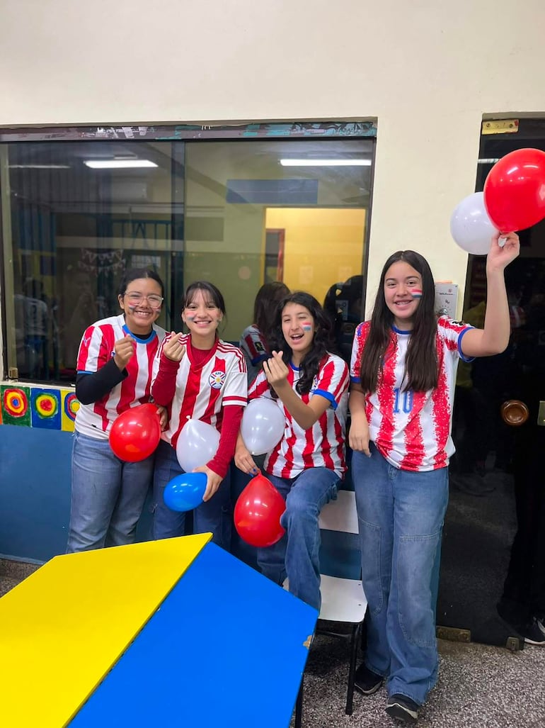 Cuatro jóvenes del CEPB con camisetas rojas y blancas sostienen globos, sonriendo en un ambiente festivo en su aula.