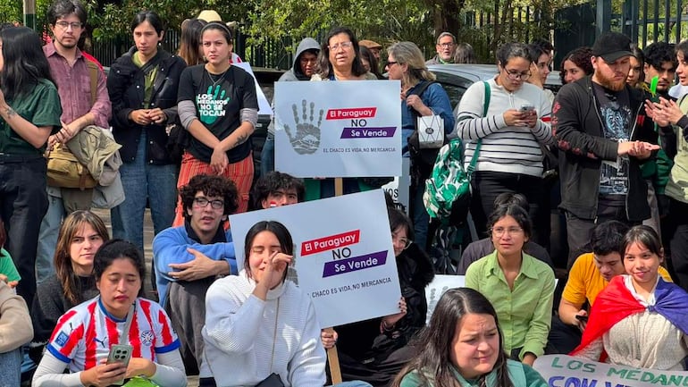 Grupo de personas sentadas en el suelo de la protesta, algunas con camisetas rojo y blanco, sosteniendo carteles de oposición.