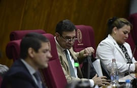 Silvio Ovelar Benitez en chaqueta oscura, sentado junto a dos personas; uno en chaqueta clara, otro en blazer blanca, todos en ambiente formal.