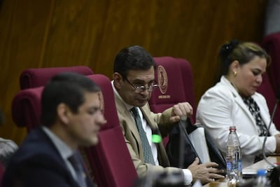 Silvio Ovelar Benitez en chaqueta oscura, sentado junto a dos personas; uno en chaqueta clara, otro en blazer blanca, todos en ambiente formal.