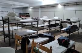 Ambiente del albergue con literas desordenadas y camas individuales. Espacio iluminado pero vacío de personas.