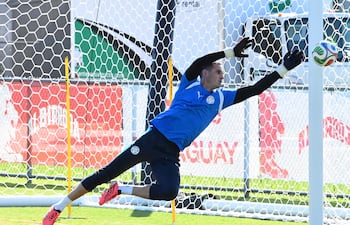 Gatito Fernández en camiseta azul y detalles blancos, estirándose para atajar un balón en práctica de fútbol al aire libre.