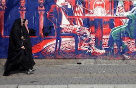 Mujeres iraníes con velo caminan junto a un mural antiestadounidense que muestra una mesa de negociaciones en una calle de Teherán, Irán, el 5 de febrero de 2026.