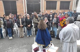 Grupo de jubilados con abrigo asiste a misa al aire libre frente a un altar sencillo, un hombre en hábito religioso dirige el acto.