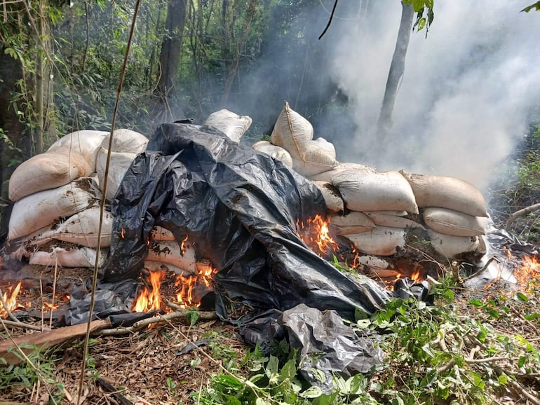 Fuego activo en vegetación junto a bolsas cubiertas de plástico negro, indicios de acción contra el narcotráfico.