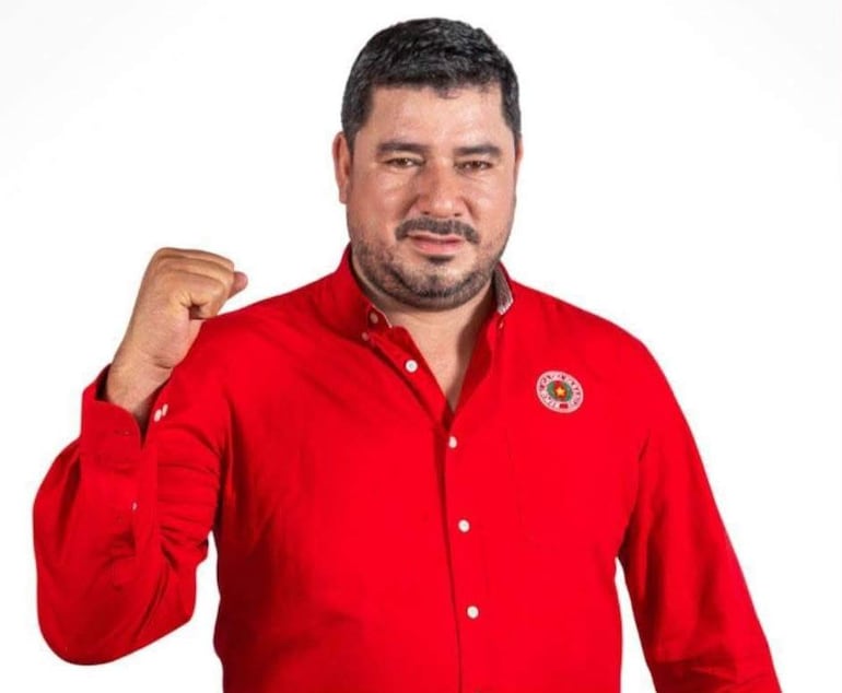 Carlos Benítez con camisa roja, brazo en alto y expresión decidida, posando frente a fondo neutro.