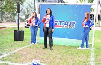 Mujeres en camisetas de la bandera paraguaya, una oradora sostiene micrófono, balón de fútbol en el suelo.