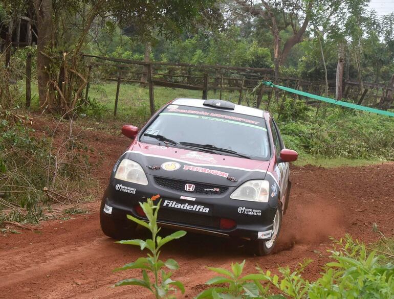 Automóvil Honda rojo y negro corriendo en un camino rural, levantando polvo y con patrocinadores visibles en la carrocería.