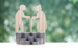 Figuras de madera representando a ancianos parados sobre unas pilas de monedas.