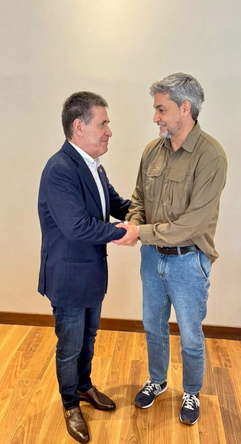 Cartes, con saco oscuro y camisa blanca, y Abdo Benítez, en camisa clara y jeans, se saludan sonriendo en un ambiente interior.