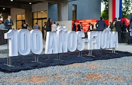Multitud de personas vestidas formalmente celebrando el centenario de FIUNA, junto a un cartel conmemorativo en un entorno urbano.