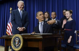 El entonces presidente estadounidense Barack Obama (c) bromea con una niña por el hecho de ser zurdo mientras firma 23 órdenes ejecutivas para endurecer el control de armas junto al vicepresidente Joe Biden (i) en Washington, Estados Unidos, en una foto de archivo fechada el 16 de enero de 2013.
