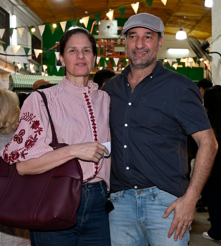 Mujer con blusa de rayas rojas y blancas y hombre con gorra gris sonríen en un ambiente festivo con decoraciones de banderines.