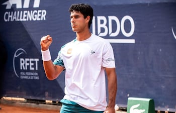 Daniel Vallejo, en camiseta blanca y pantalones cortos verdes, levanta la mano en celebración en la cancha de tenis.