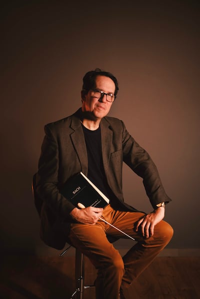 Diego Sánchez Haase sentado en un taburete con chaqueta gris oscuro y camiseta negra, sosteniendo un libro titulado 'Bach'.
