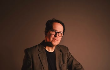 Diego Sánchez Haase sentado en un taburete con chaqueta gris oscuro y camiseta negra, sosteniendo un libro titulado 'Bach'.