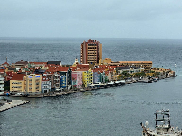 Vista del puerto de Willemstad con edificios de colores vibrantes y un barco anclado en un día nublado.