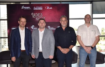 Cuatro hombres en trajes posan frente a un cartel de 'LADIES NIGHT', en un entorno luminoso con logotipos de sponsors.