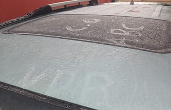 Techo de un vehículo cubierto de gotas de lluvia, en un entorno exterior con fondo rojizo.