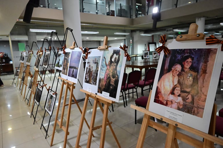 Exposición en espacio iluminado con fotografías en caballetes decorados con cintas de colores.