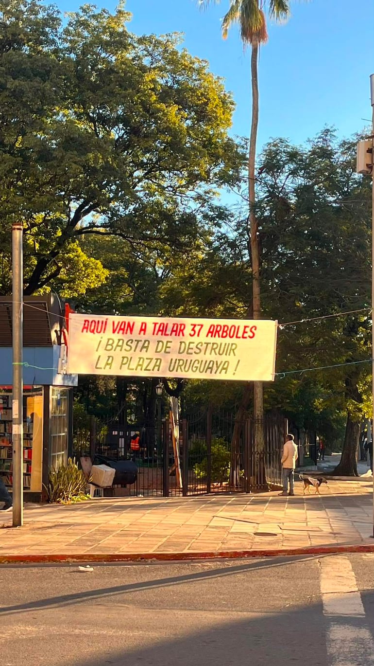 Hombre de pie junto a un perro, sosteniendo un cartel que dice '¡BASTA DE DESTRUIR LA PLAZA URUGUAYA!'.