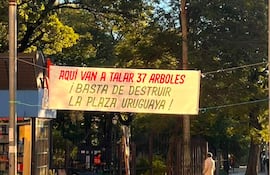 Hombre de pie junto a un perro, sosteniendo un cartel que dice '¡BASTA DE DESTRUIR LA PLAZA URUGUAYA!'.