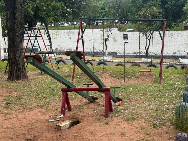 Parque infantil con tobogán verde y rojo y columpio, vacío, con césped y tierra alrededor, en un ambiente tranquilo.